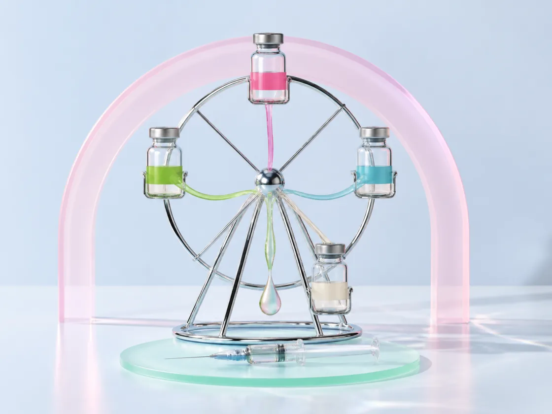 Four unlabelled glass vials in green, pink, blue and cream riding a chrome ferris wheel, their contents running together into a single drop above a syringe